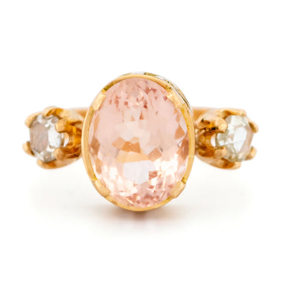 A three stone oval morganite and diamond ring in yellow gold, on a white background