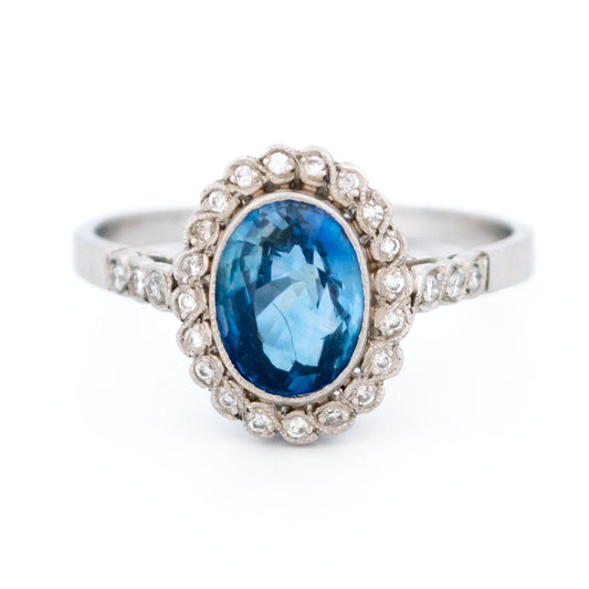 An oval sapphire and diamond cluster ring in platinum, on a white background