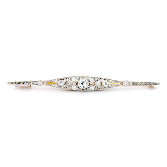 A diamond bar brooch in gold and platinum, on a white background
