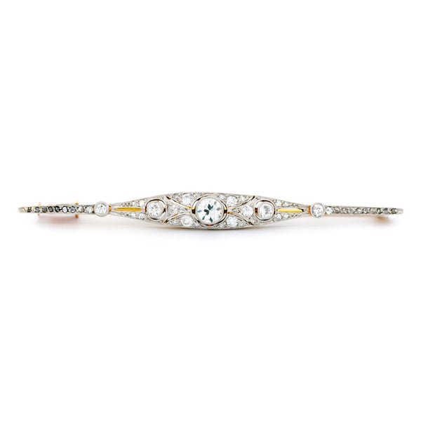 A diamond bar brooch in gold and platinum, on a white background