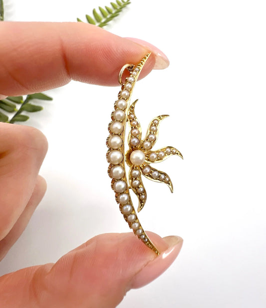 A yellow gold pearl set cresent and sunburst pendant, held in a hand