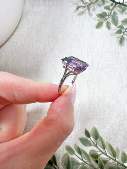 A solitaire amethyst cocktail ring in platinum, held in a hand