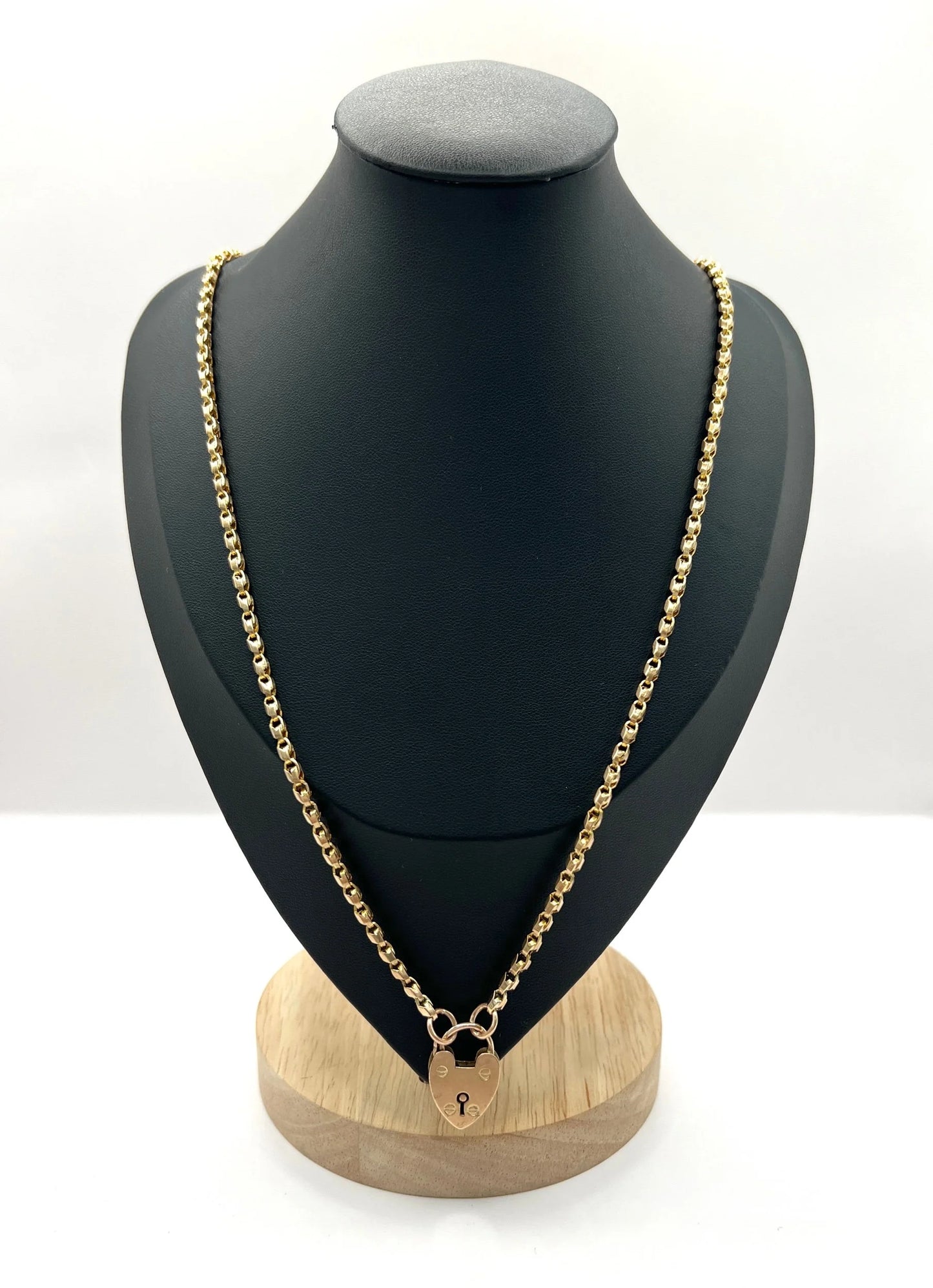 A gold chain necklace withgold heart padlock, modelled on a black bust