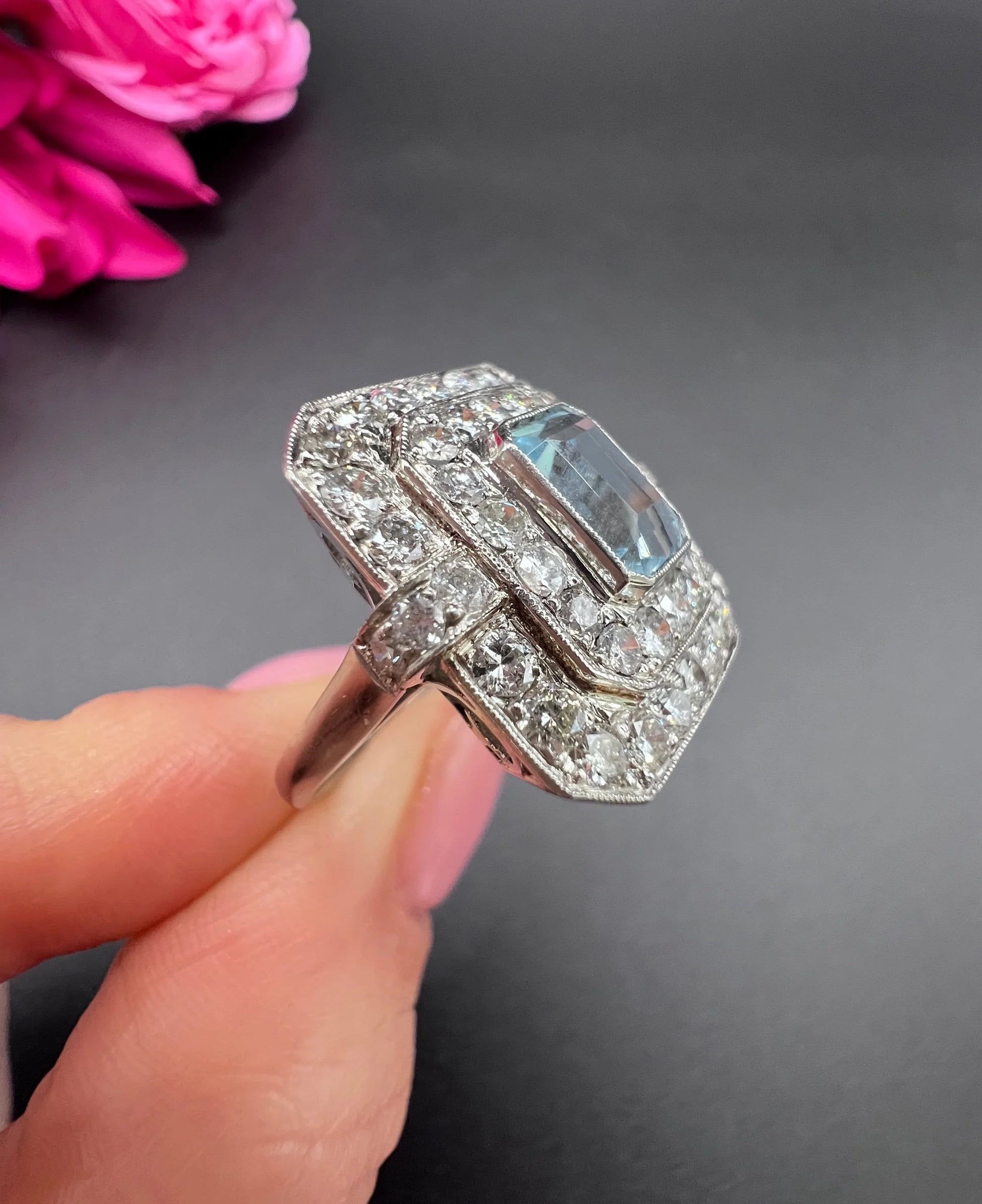An octagonal shaped cluster ring with an aquamarine centre surrounded by two rows of diamonds, in platinum, held in a hand