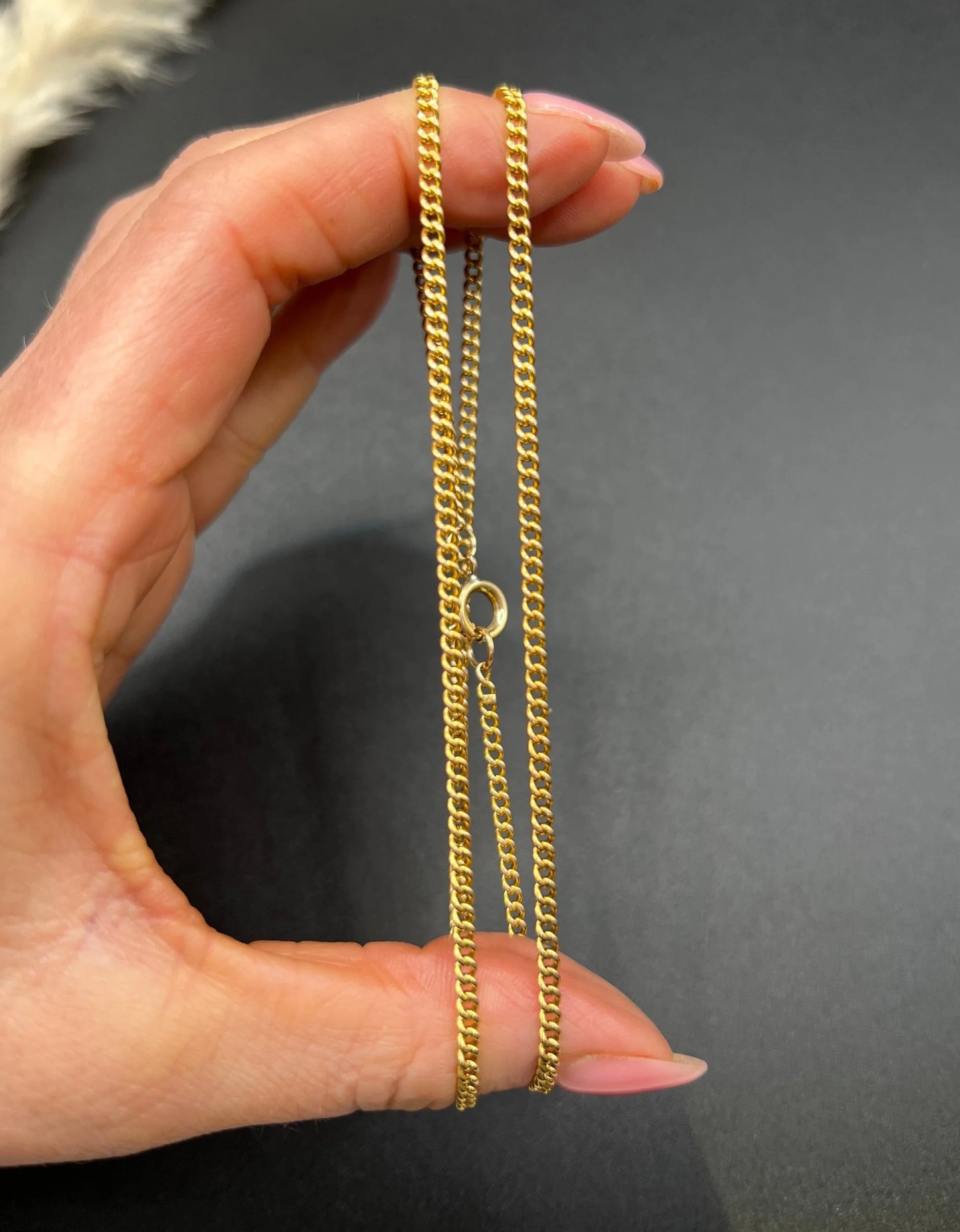 A fine curb link chain necklace in yellow gold, held in a hand