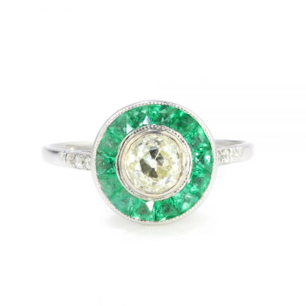 Old Cut Diamond and Emerald Cluster Target Ring; 0.45ct old-cut diamond within calibre-cut emerald surround, diamond accents to the shoulders. Circa 1920s.
