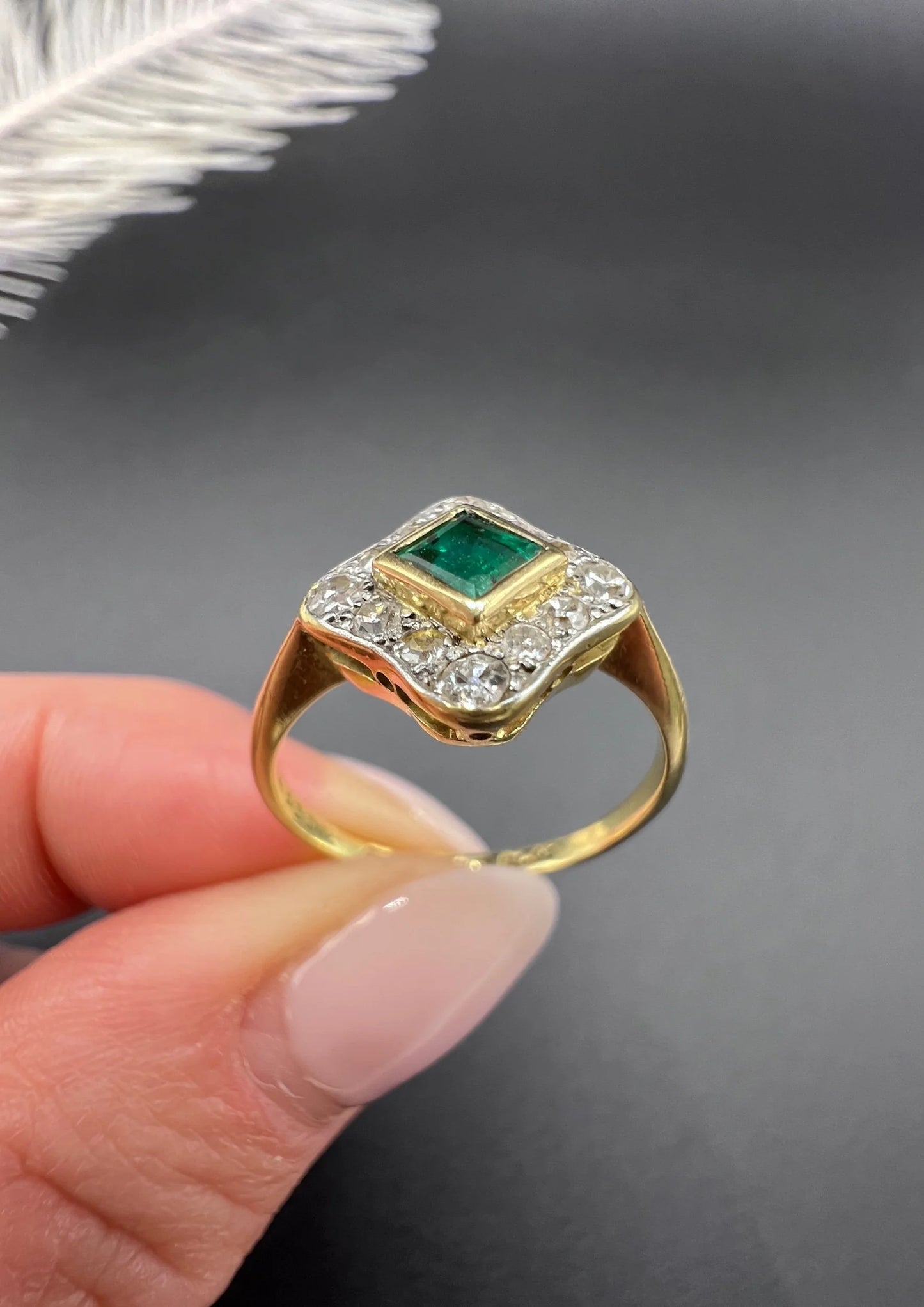An emerald and diamond cluster ring in yellow gold and platinum, held in a hand