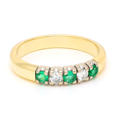 A yellow and white gold five stone ring with emeralds and diamonds, against a white background