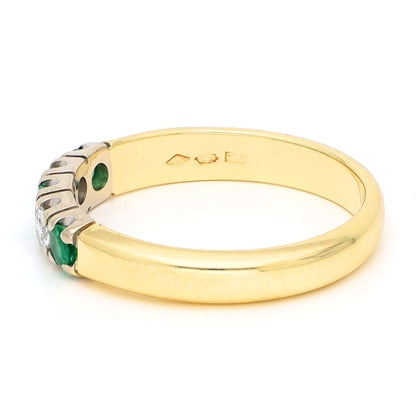 A yellow and white gold five stone ring with emeralds and diamonds, against a white background