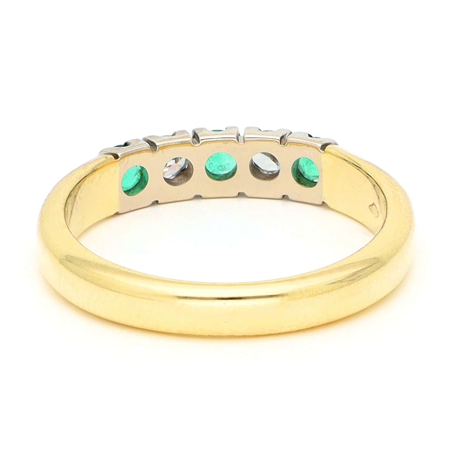 A yellow and white gold five stone ring with emeralds and diamonds, against a white background