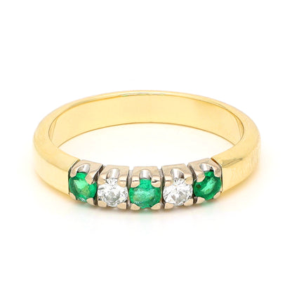 A yellow and white gold five stone ring with emeralds and diamonds, against a white background