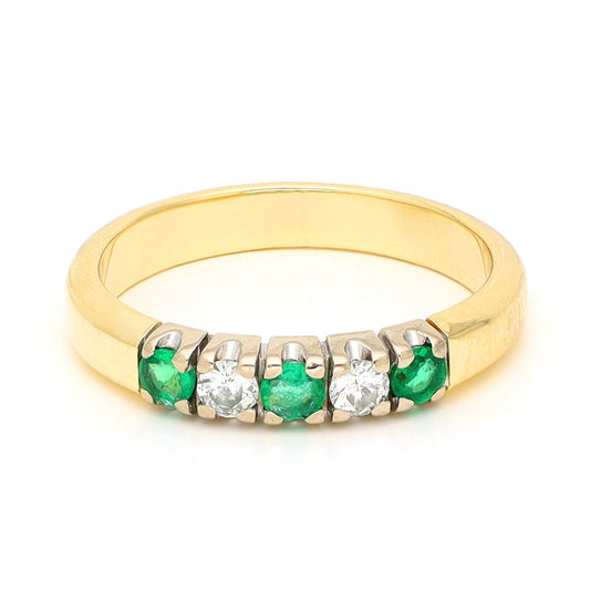 A yellow and white gold five stone ring with emeralds and diamonds, against a white background