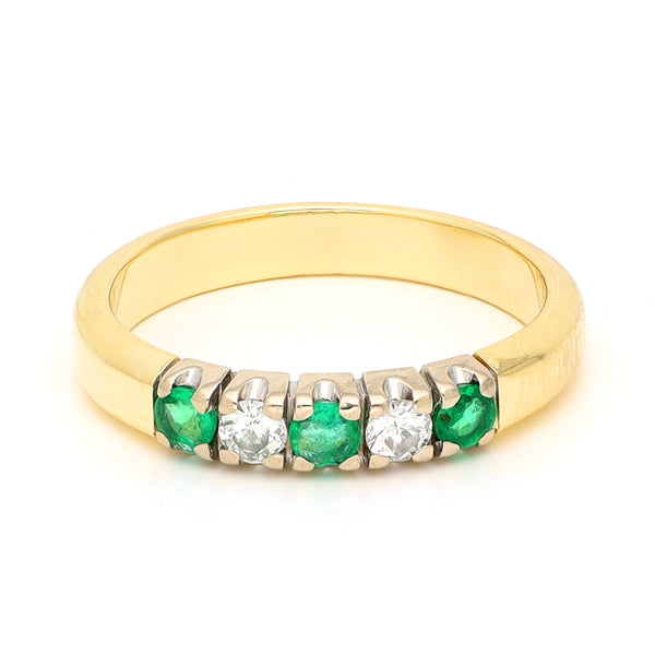 A yellow and white gold five stone ring with emeralds and diamonds, against a white background
