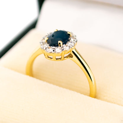 An oval sapphire and round diamond cluster ring in yellow and white gold, in a ring box