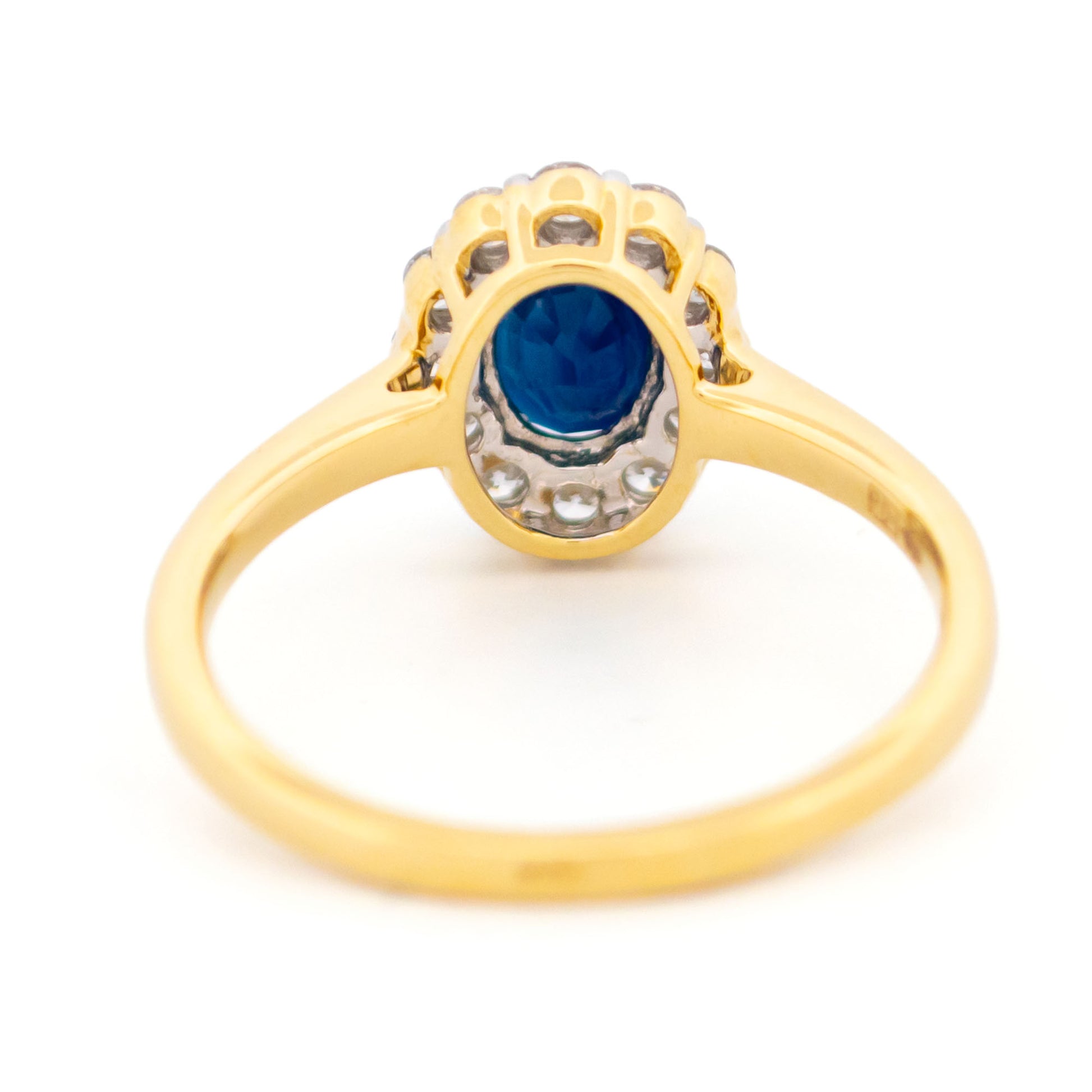 An oval sapphire and round diamond cluster ring in yellow and white gold, against a white background