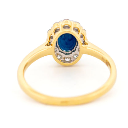 An oval sapphire and round diamond cluster ring in yellow and white gold, against a white background