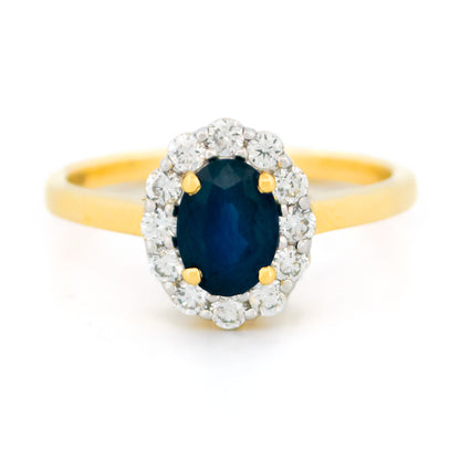 An oval sapphire and round diamond cluster ring in yellow and white gold, against a white background