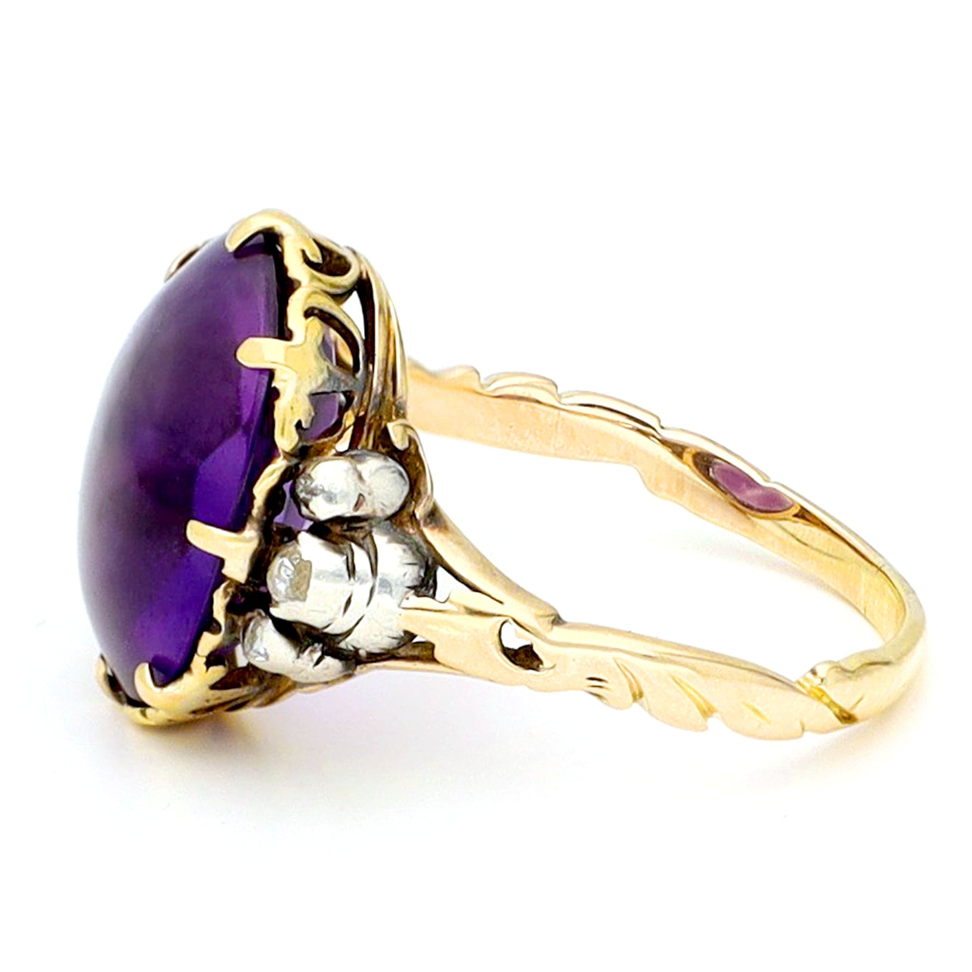 A buff top, oval shaped amethyst ring with rose cut diamond shoulders in yellow and white gold, against a white background