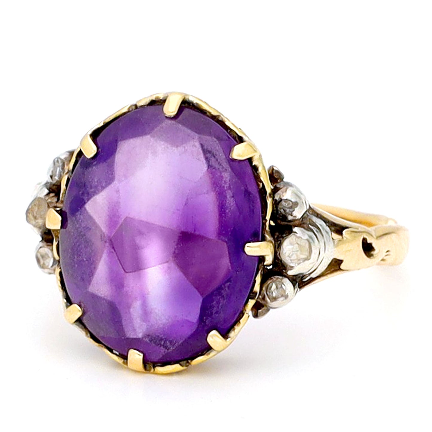 A buff top, oval shaped amethyst ring with rose cut diamond shoulders in yellow and white gold, against a white background