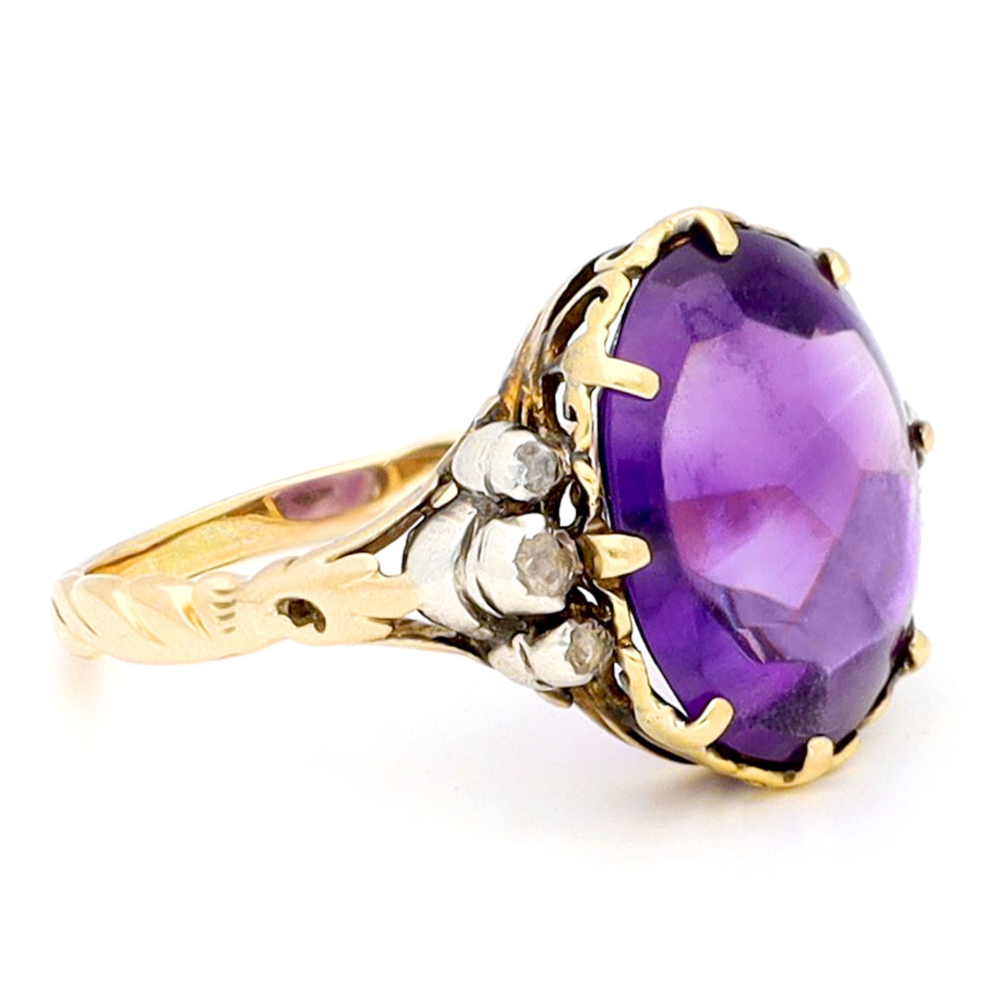 A buff top, oval shaped amethyst ring with rose cut diamond shoulders in yellow and white gold, against a white background