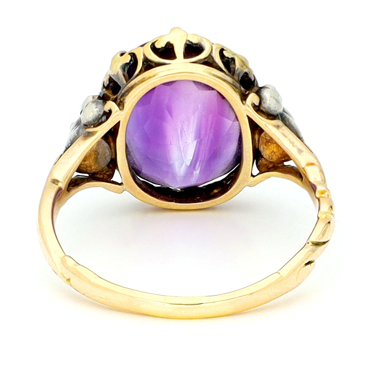 A buff top, oval shaped amethyst ring with rose cut diamond shoulders in yellow and white gold, against a white background