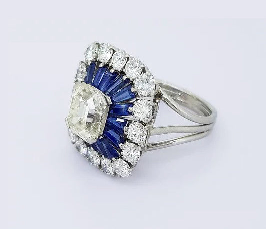 Vintage 2.30ct Emerald Cut Diamond and Sapphire Cluster Cocktail Ring; 2.30 carat emerald-cut diamond, surrounded by tapered calibre-cut sapphires and 3.00cts brilliant-cut diamonds