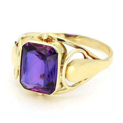 A yellow gold emerald cut amethyst ring, against a white background