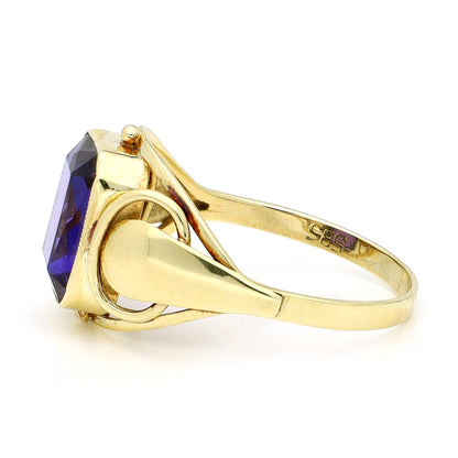 A yellow gold emerald cut amethyst ring, against a white background