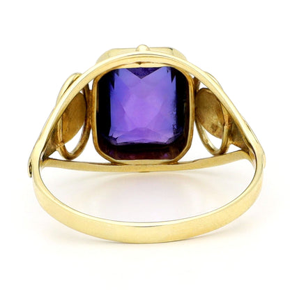 A yellow gold emerald cut amethyst ring, against a white background