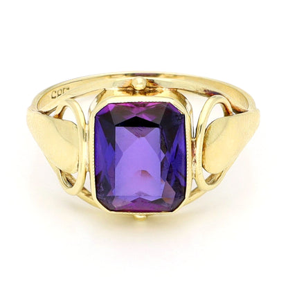 A yellow gold emerald cut amethyst ring, against a white background