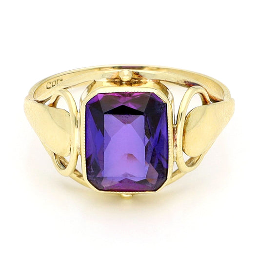 A yellow gold emerald cut amethyst ring, against a white background