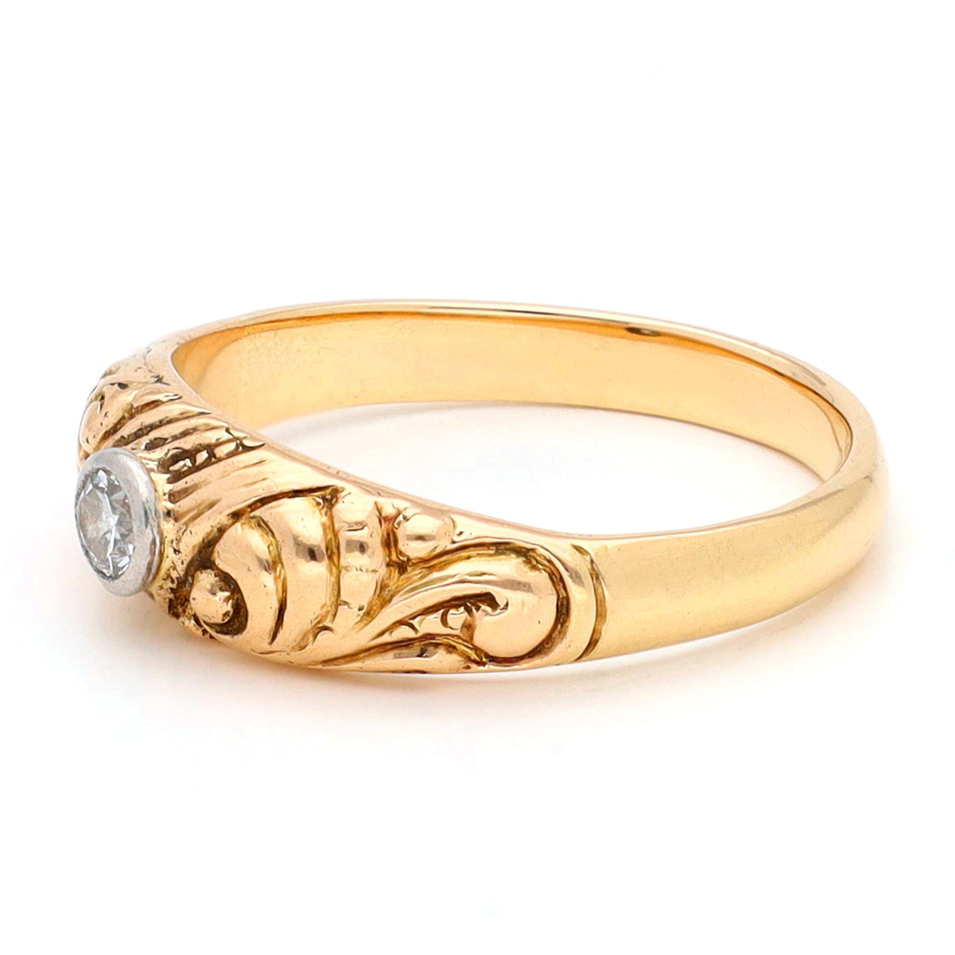 A yellow gold ring with a single old cut diamond bezel set in white gold, with scroll engraving, against a white background