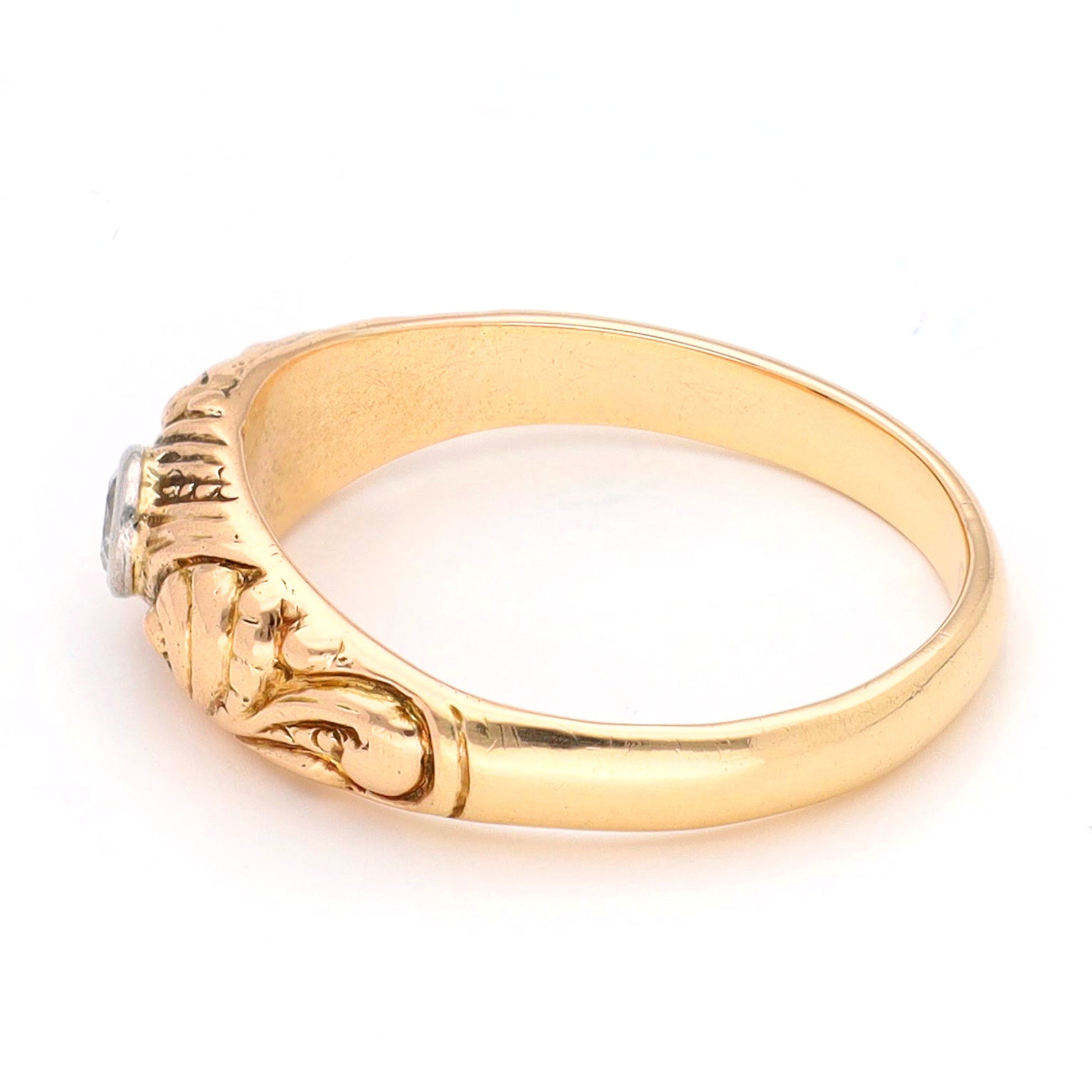 A yellow gold ring with a single old cut diamond bezel set in white gold, with scroll engraving, against a white background