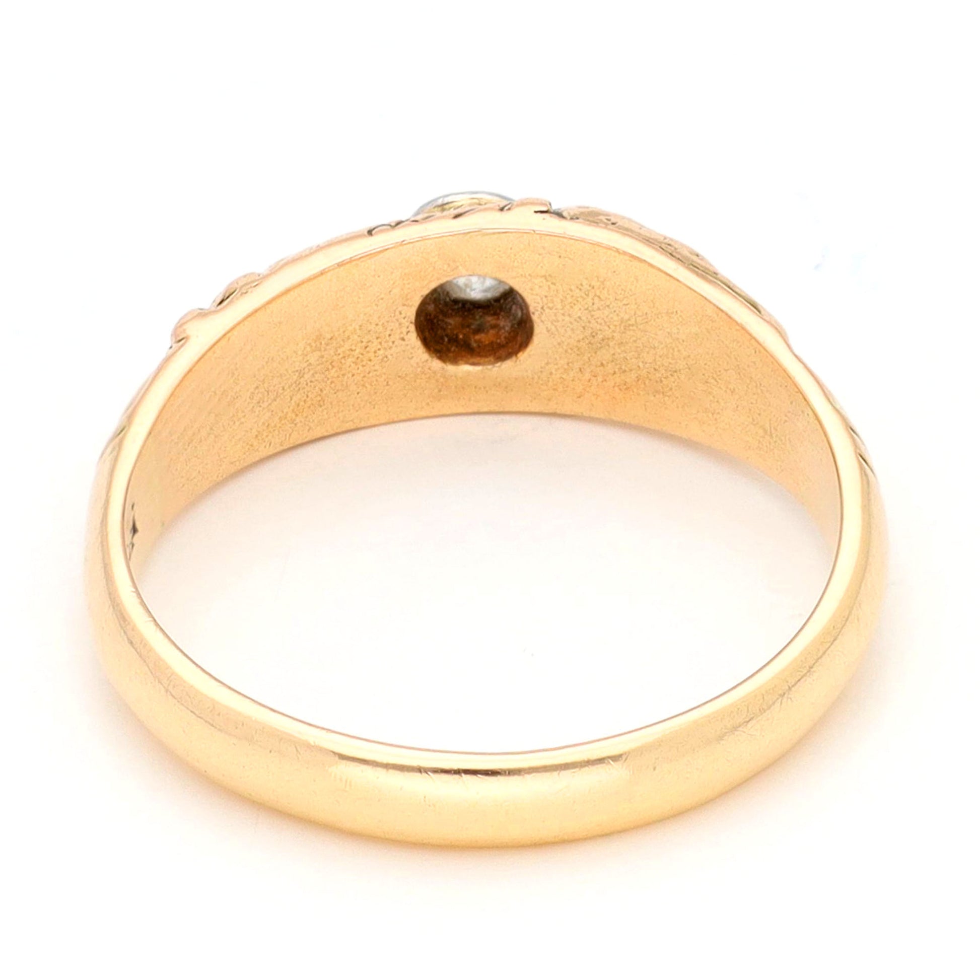 A yellow gold ring with a single old cut diamond bezel set in white gold, with scroll engraving, against a white background