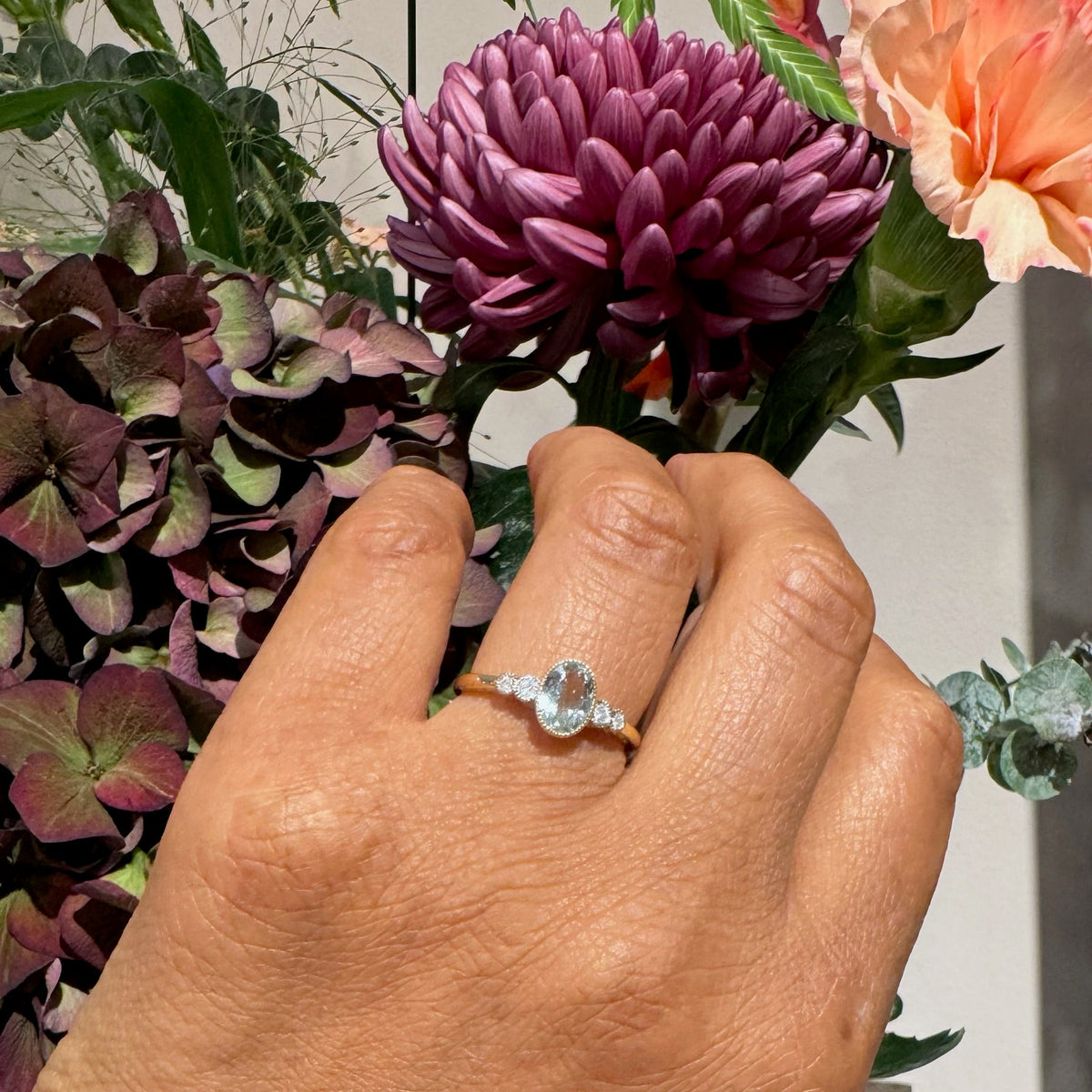 An oval aquamarine and round diamond ring in yellow and white gold, modelled on a hand