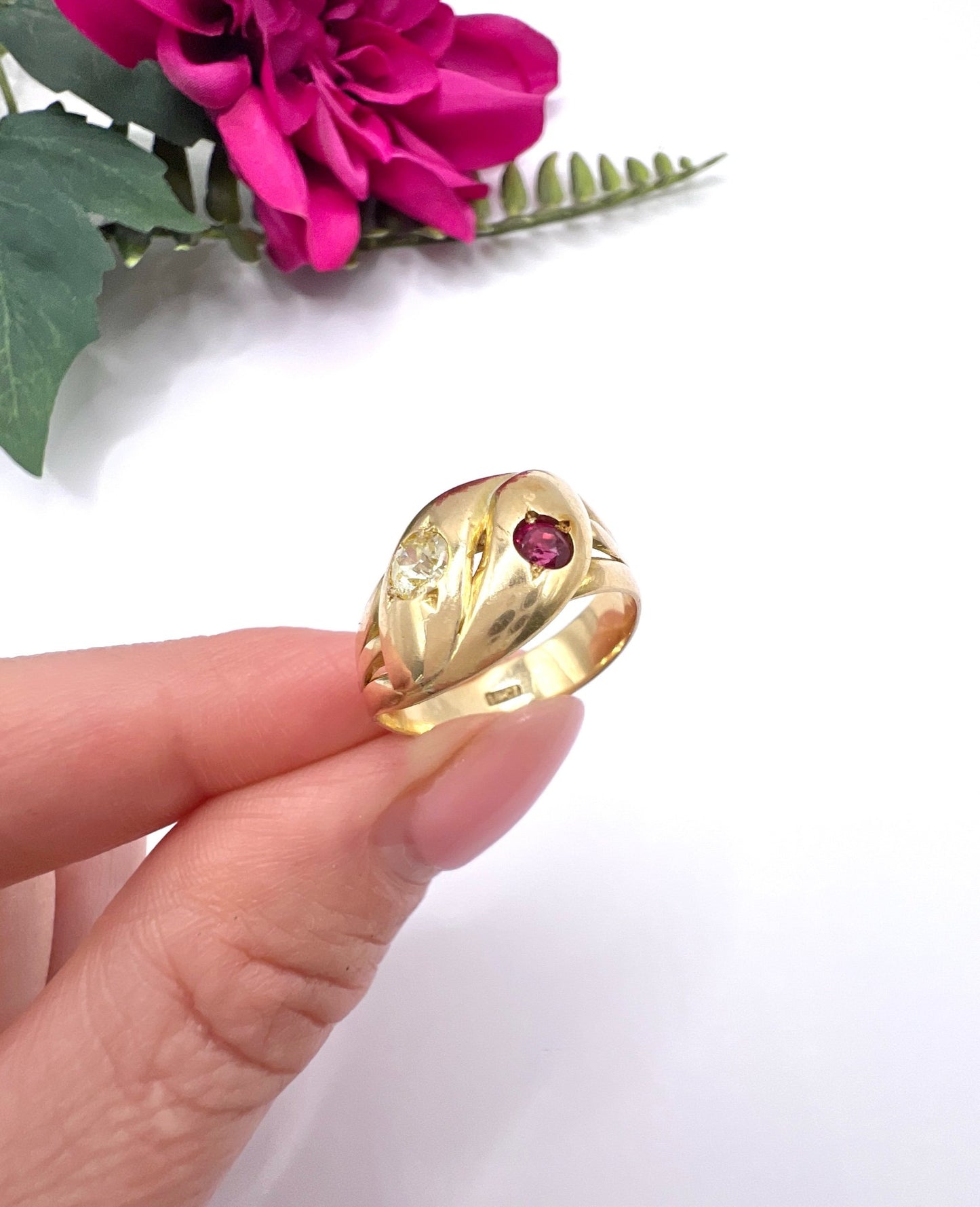 A yellow gold double headed snake ring with a ruby and a diamond, held in a hand