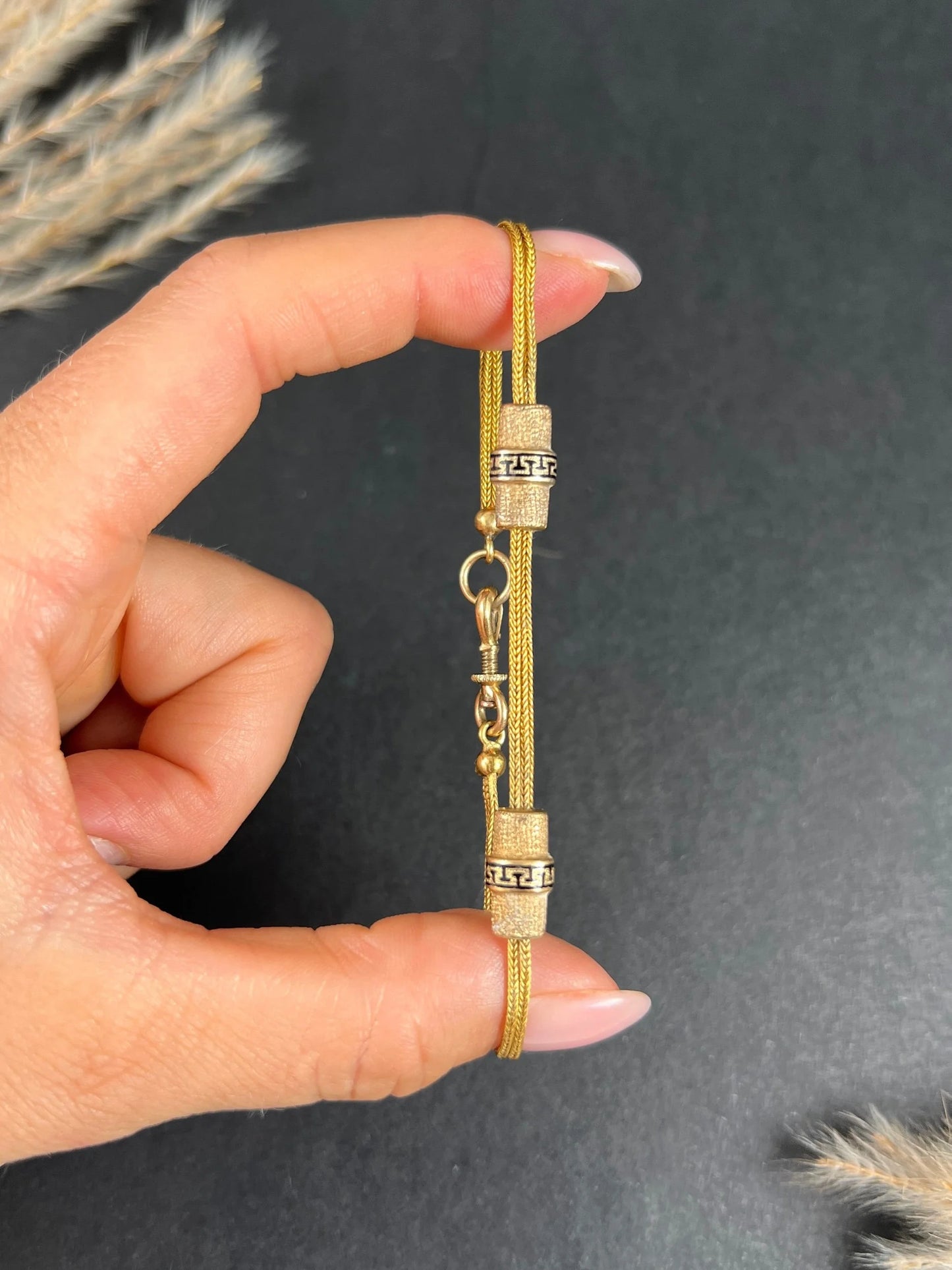 A yellow gold double row bracelet with black enamel tubular beads, held in a hand