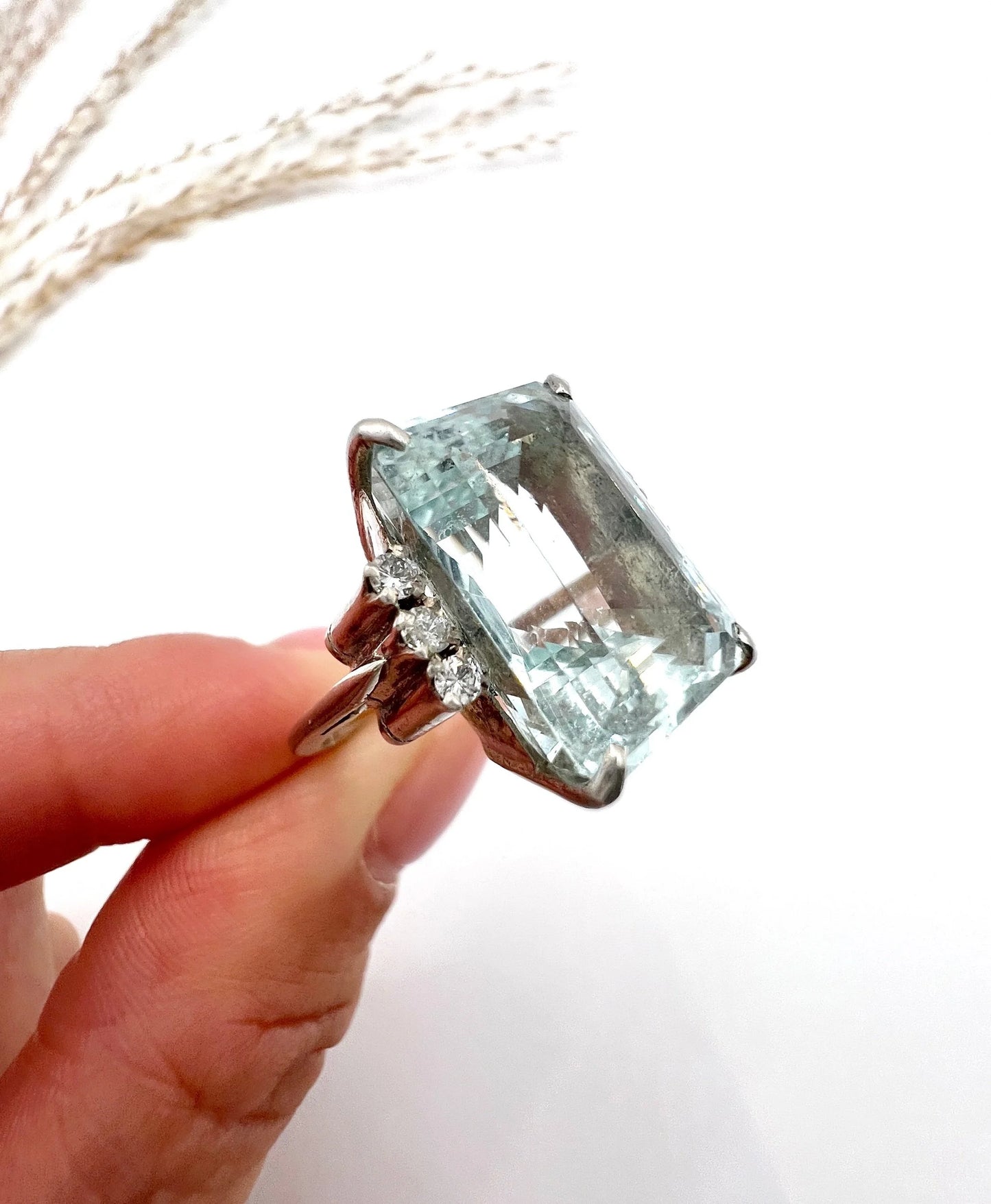 An aquamarine and diamond cocktail ring in white gold, held by a hand