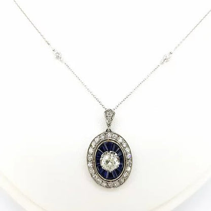 Sapphire and Diamond Oval Cluster Pendant on Diamond Set Chain; central brilliant cut diamond surrounded by calibre cut sapphires and an outer halo of diamonds