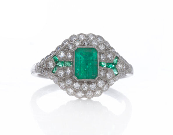 Art Deco Style Emerald, Diamond and Platinum Cluster Dress Ring; central emerald-cut emerald surrounded by brilliant-cut diamonds and accented by calibre-cut emerald set shoulders. Circa 1980s