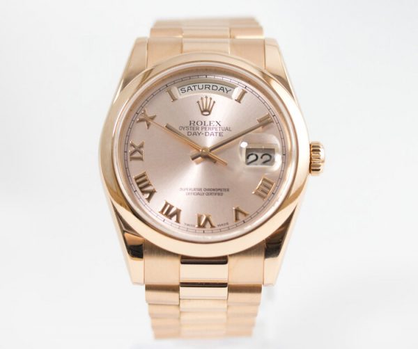 Rolex Day Date 18ct Pink Gold 118205 Automatic Watch; 36mm case with pink dial, Roman numerals, magnified quick-set date and a weekday aperture, on a matching 18ct pink gold Rolex President bracelet, Rolex green protection sticker present on the case back. In mint condition and comes with Rolex box