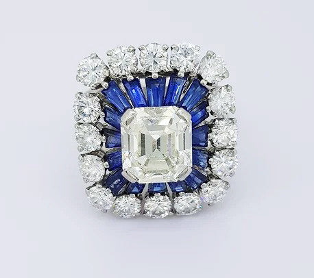 2.30ct Emerald Cut Diamond and Sapphire Cluster Cocktail Ring; 2.30 carat emerald-cut diamond, surrounded by calibre-cut sapphires and 3.00cts diamonds