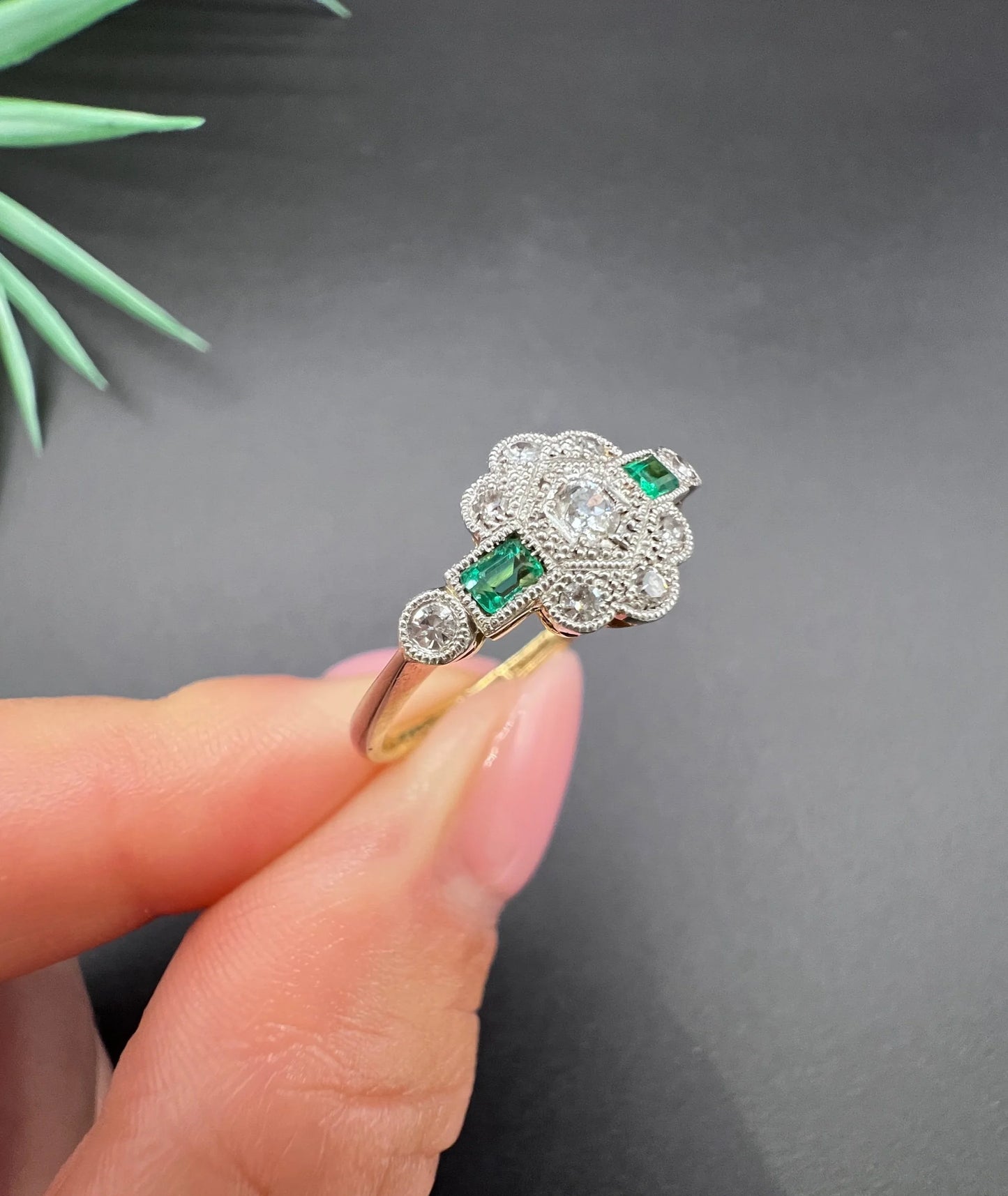 An emerald and diamond floral cluster ring in yellow gold and platinum, held in a hand
