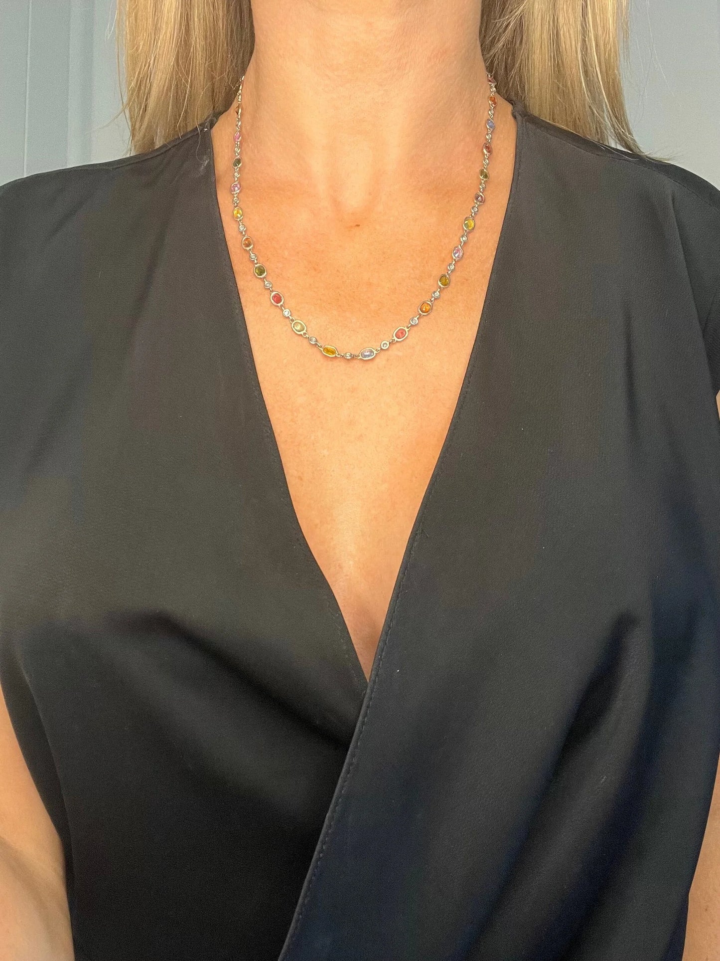 A coloured sapphire and diamond set necklace in platinum and gold, modelled by a lady wearing a black top