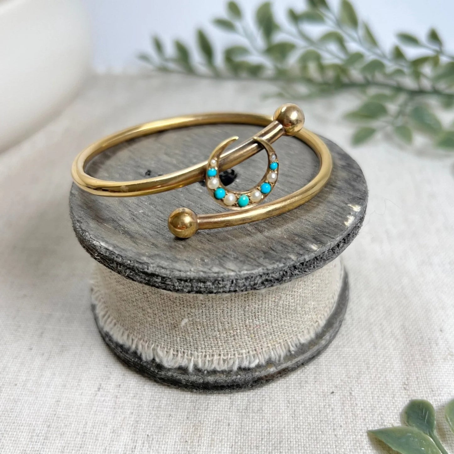 A yellow gold crossover bangle bracelet with a pearl and turquoise crescent moon centre