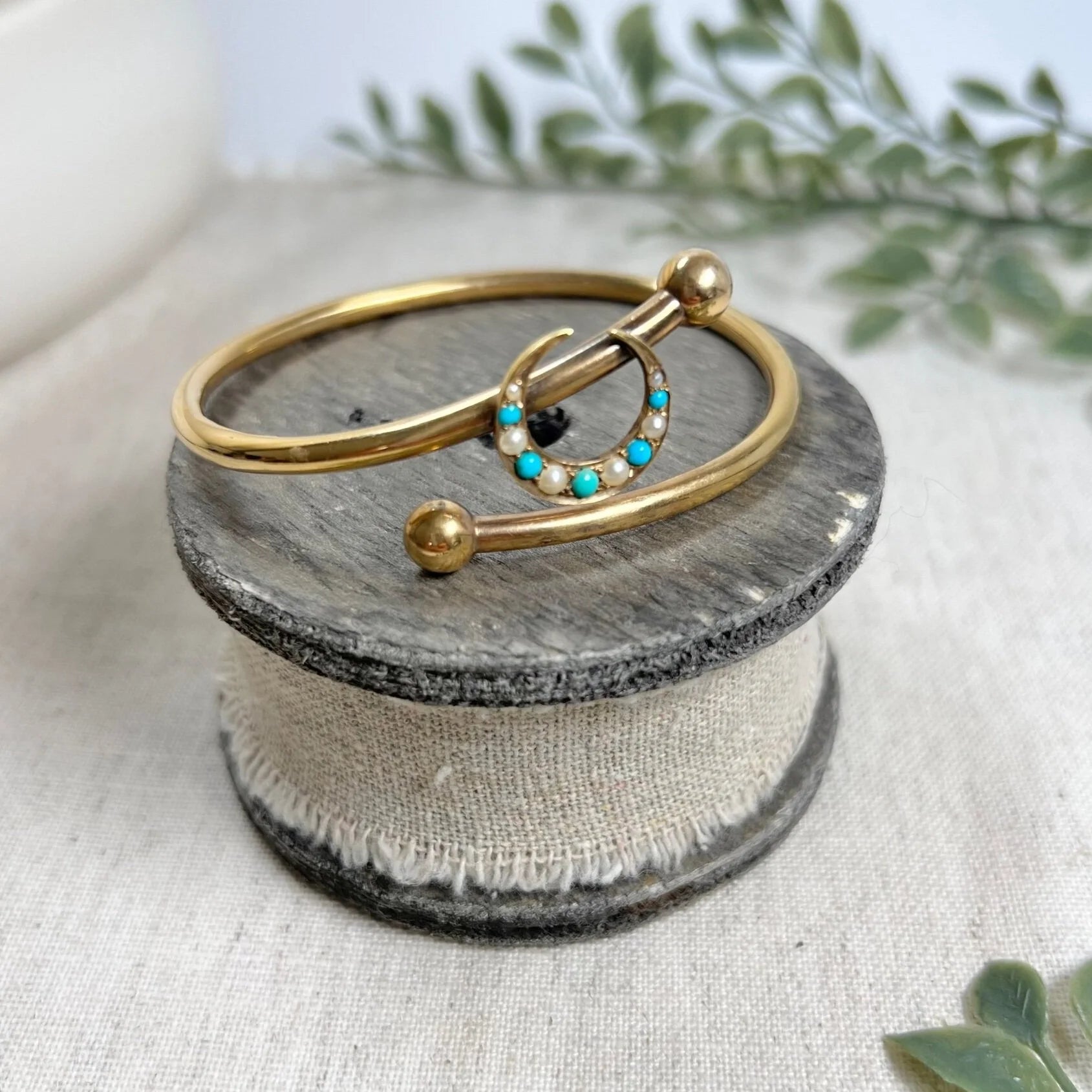 A yellow gold crossover bangle bracelet with a pearl and turquoise crescent moon centre