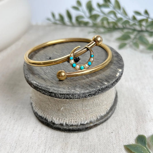 A yellow gold crossover bangle bracelet with a pearl and turquoise crescent moon centre