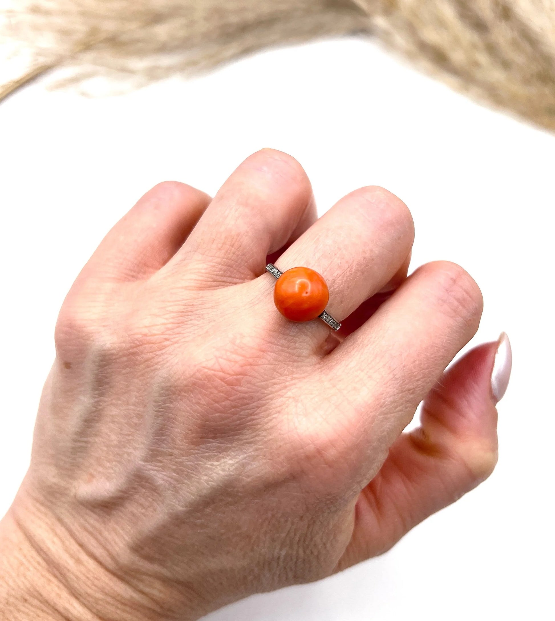 A round orange coral and diamond dress ring in platinum, modelled on a hand