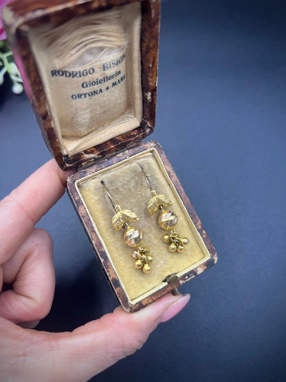 A pair of yellow gold leaf and faceted ball drop earrings with hook fittings, in an antique box, held in a hand