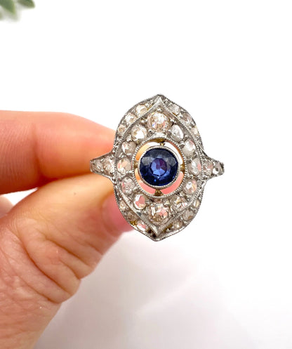 A sapphire and diamond openwork ring in platinum with a yellow gold ring shank, held in a hand